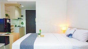 A hotel room with a bed, bedside table, lamp, and a view of the kitchen area. - Relaxing Stay Studio At Apartment Lrt City Bekasi (Bekasi)