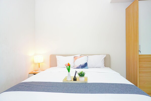 A neatly made bed with a white and blue blanket, a bedside lamp, a vase with flowers, and a tray with a plant and a candle. - Relaxing Stay Studio At Apartment Lrt City Bekasi (Bekasi)