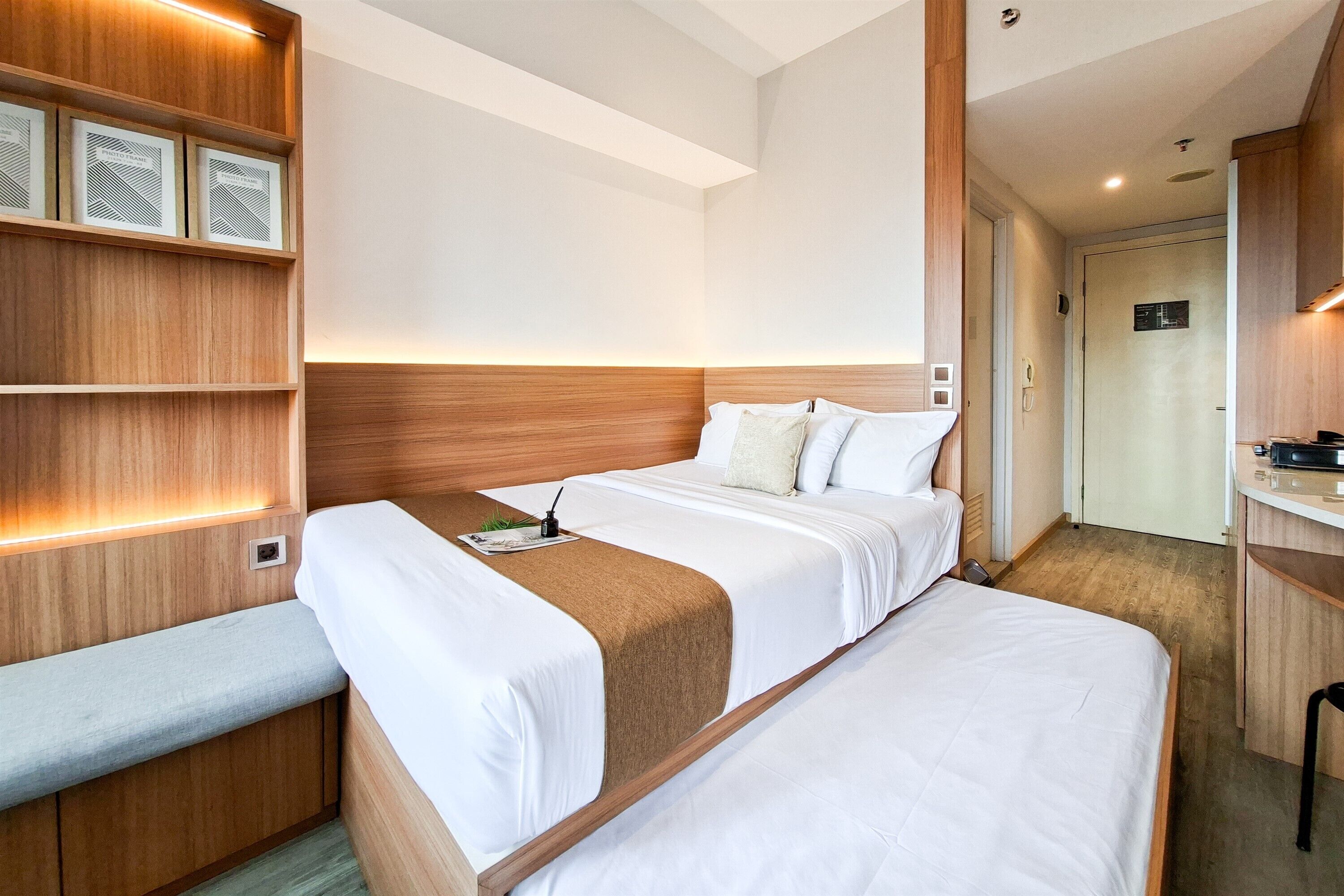 A modern hotel room with a large bed, a bedside table, a bench, and a wooden headboard.