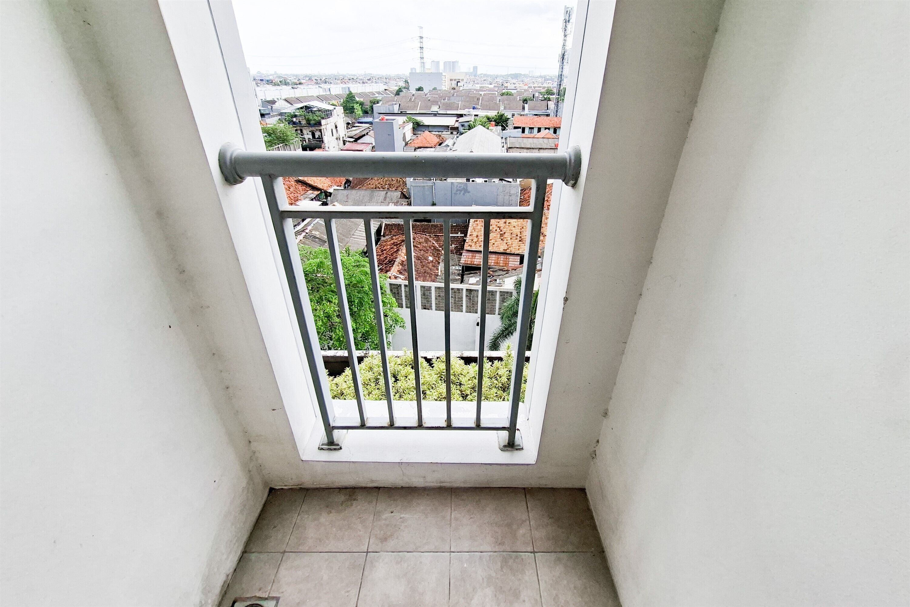 A balcony with a metal railing, a tiled floor, and a view of buildings and greenery.