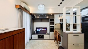 A modern kitchen with a built-in TV, wooden cabinetry, and a dining area with chairs. - Functional 2Br With Extra Room At M-Town Residence (Gading Serpong)