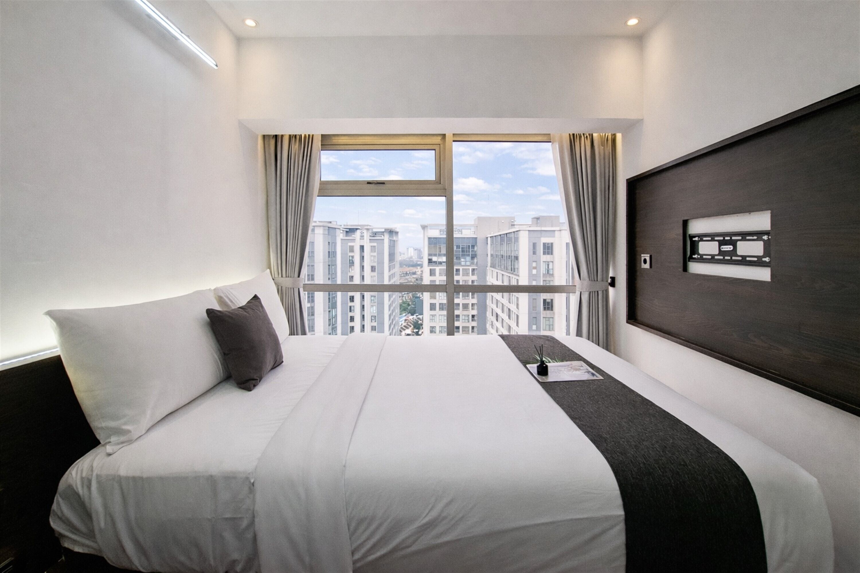 A hotel room with a large bed, a view of the city through a window, and a dark wood headboard.