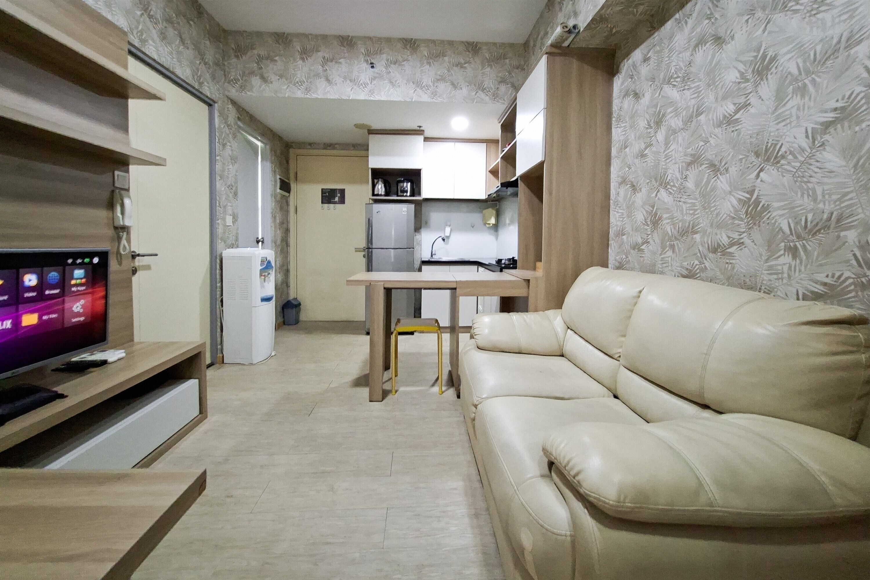 A living room with a sofa, a TV, a small table, and a kitchen area in the background.