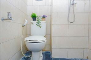 A bathroom with a toilet, a shower, and two potted plants on the toilet tank. - Cozy And Pleasant Studio At Apartment Margonda Residence 1 (Depok)