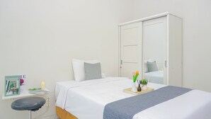 Ein Hotelzimmer mit einem Bett, einem Schreibtisch, einem Stuhl, einem Kleiderschrank und einem kleinen Regal mit einem Buch und einer Kerze.