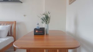 A wooden table with a water bottle and a travel bag, a white sofa with a pillow, and a vase with green foliage. - Serene Studio Apartment At Margonda Residence 2 (Depok)
