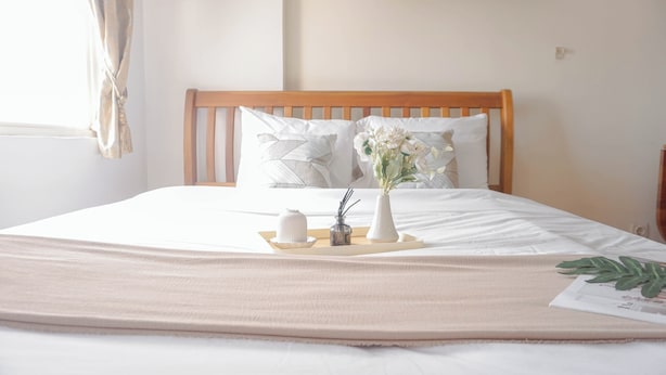 A neatly made bed with a wooden headboard, white bedding, and a tray with a vase of flowers. - Serene Studio Apartment At Margonda Residence 2 (Depok)