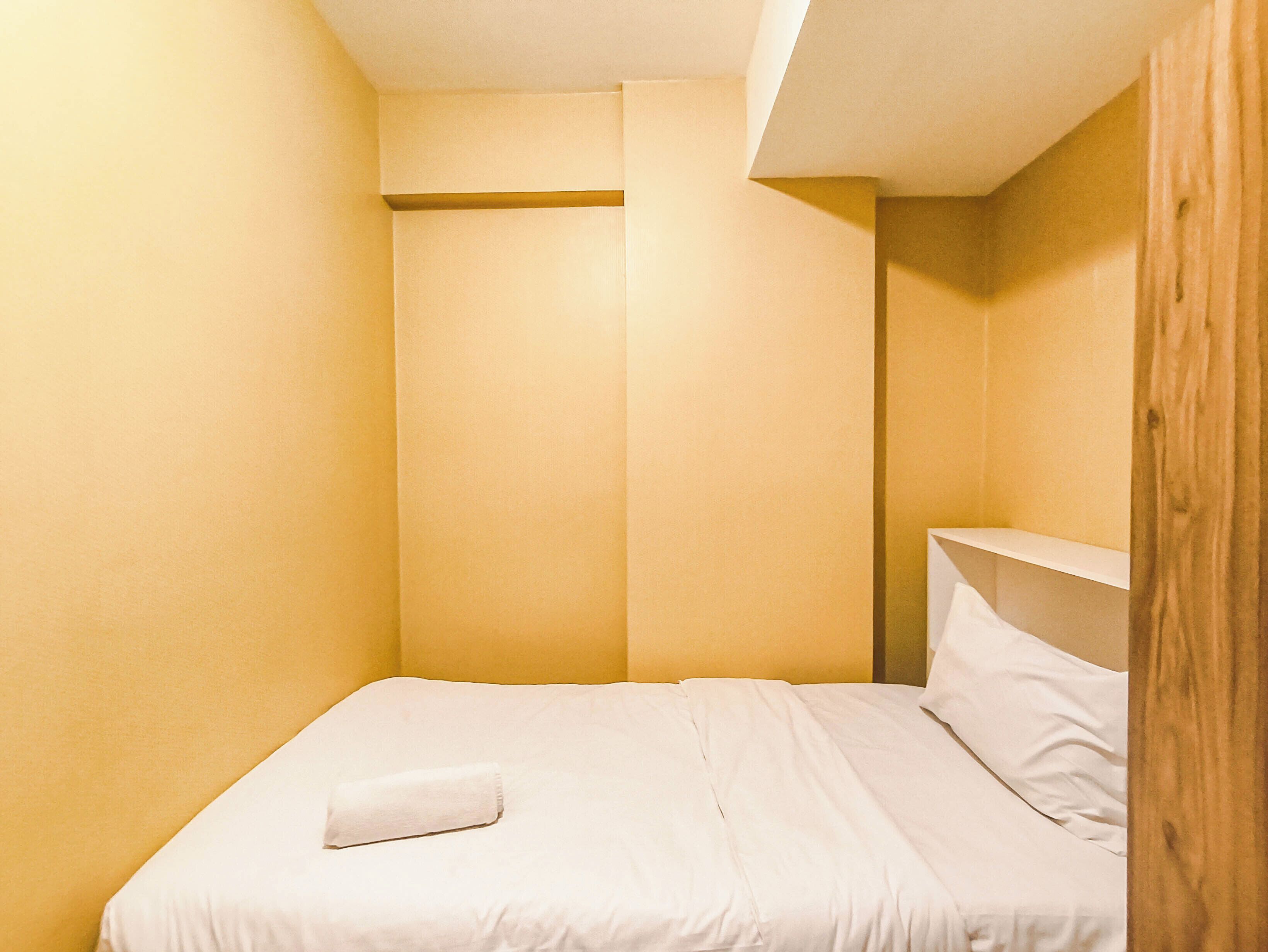Une petite chambre avec un lit simple, une tête de lit en bois, un oreiller blanc et une étagère en bois.