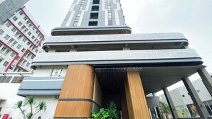 A modern high-rise building with a prominent entrance featuring a wooden column and a covered walkway. - Wooden Accents Studio At Monroe Tower Apartment (Cikarang)