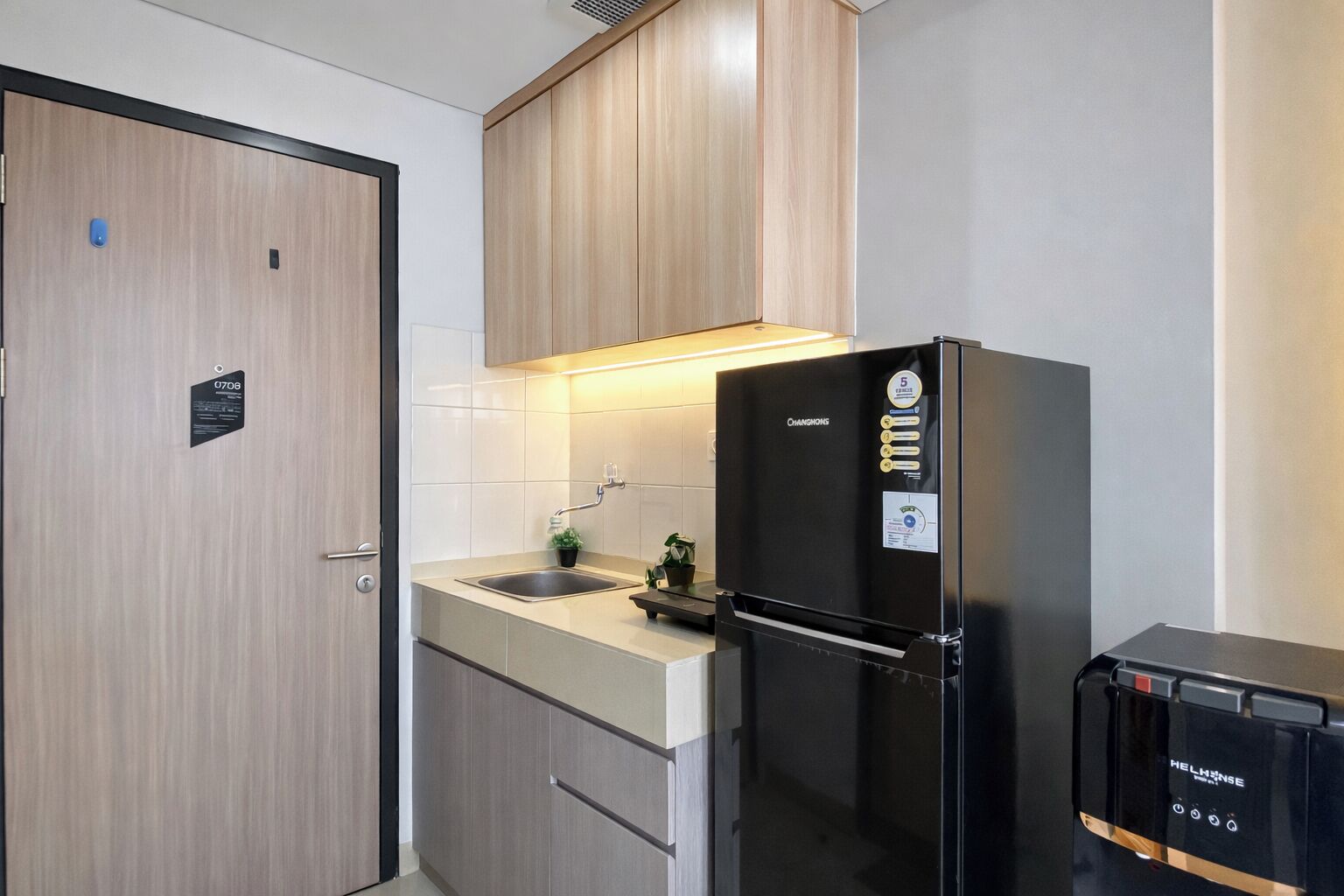 Une cuisine compacte dotée de meubles en bois, d’un évier en acier inoxydable, d’un réfrigérateur noir et d’un ensemble d’appareils électroménagers noirs.