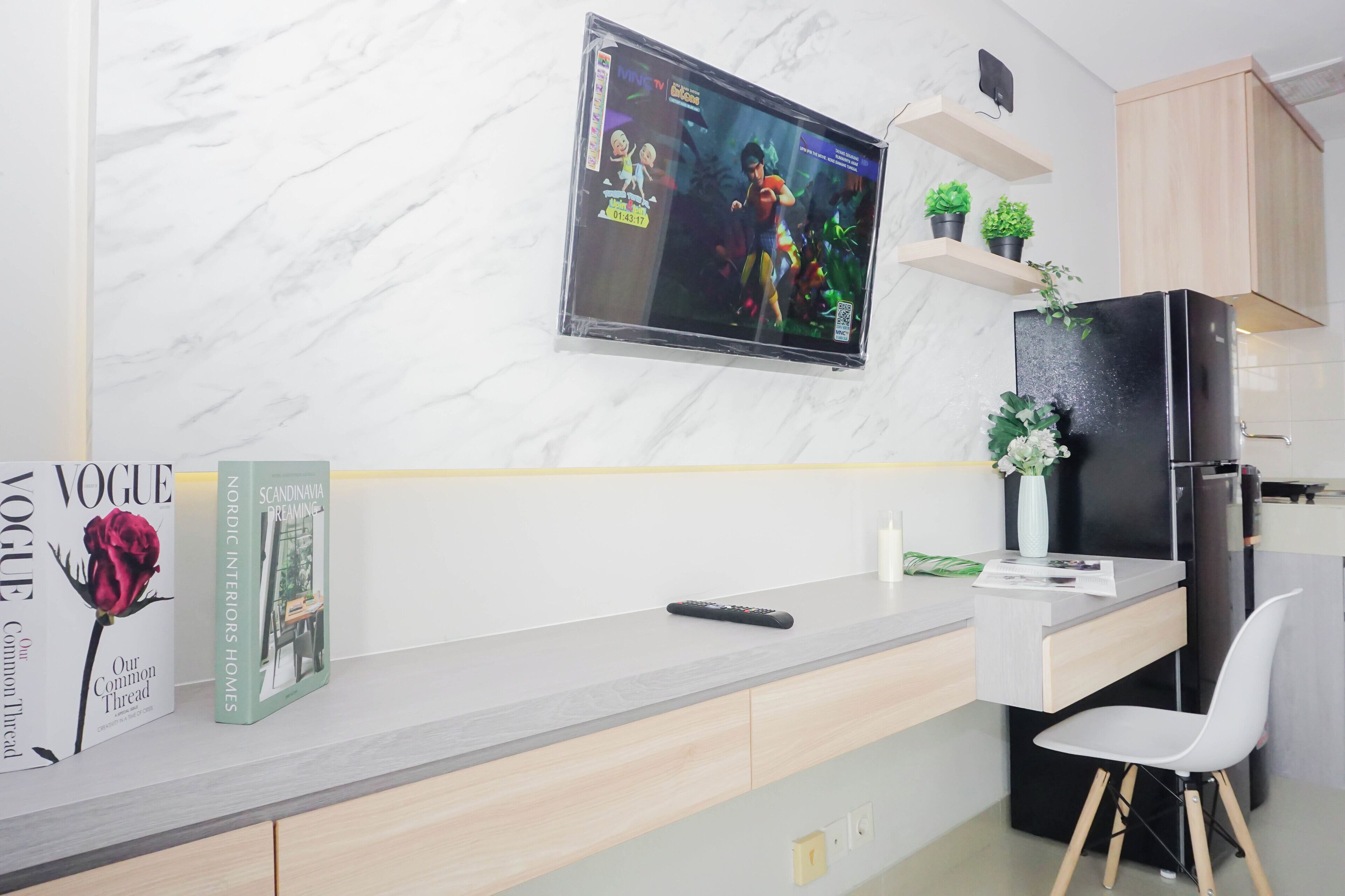 A modern kitchen with a marble backsplash, a mounted TV, a refrigerator, and a white chair.