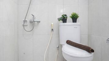 Un baño con inodoro, ducha y dos plantas en macetas detrás del inodoro.