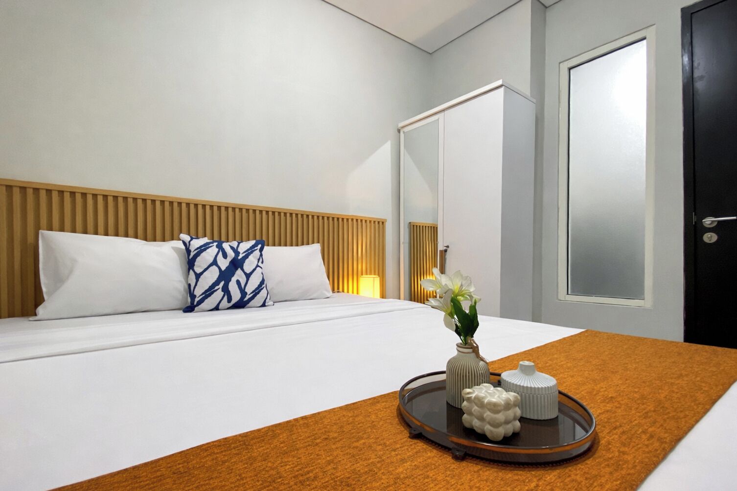 Ein Hotelzimmer mit einem Bett, einem Nachttisch mit Tablett, einer Vase mit Blumen und einem Kleiderschrank.