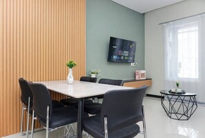A modern conference room with a large table, black chairs, a TV on the wall, and a window with blinds. - Cozy Designed 2Br Apartment For 6 Pax At Nifarro Park (Jakarta)