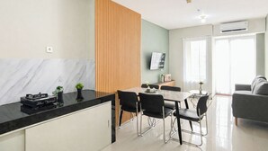 A modern kitchen with a marble countertop, a dining area with a table and chairs, a grey sofa, and a TV mounted on the wall. - Tranquil 2Br For 6 Pax At Nifarro Park Apartment (Jakarta)