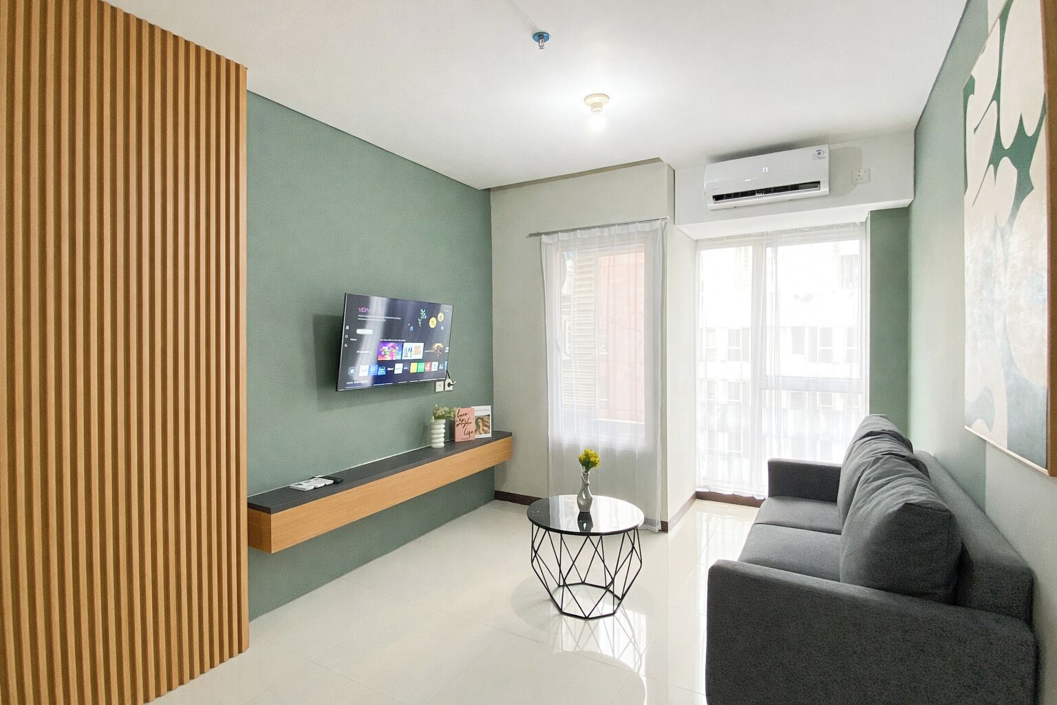 A modern living room with a flat-screen TV, a sofa, a coffee table, and a window with blinds.