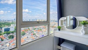 Een kamer met een groot raam, een witte kaptafel met spiegel, een klein plantje en een bank.