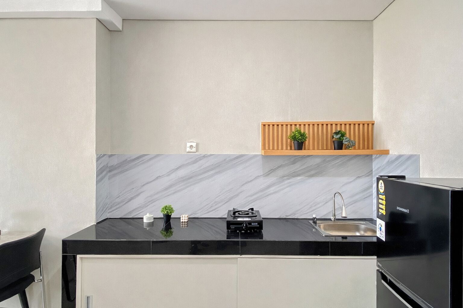 A compact kitchen with a black countertop, a built-in sink, a stove, and a wooden shelf above the countertop.
