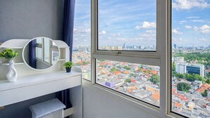 A modern room with a large window, a round mirror, a white console table, and a view of a cityscape. - Clean Space And Well Located 2Br At Nifarro Park Apartment (Jakarta)
