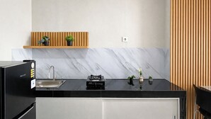 A modern kitchen with a black countertop, stainless steel sink, and a built-in stove. There are wooden shelves above the sink holding potted plants. - Comfy 2Br For 6 Pax At Nifarro Park Apartment (Jakarta)