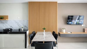A modern kitchen with a marble backsplash, a dining area with a checkered tablecloth, and a TV mounted on the wall displaying a streaming service. - Comfy 2Br For 6 Pax At Nifarro Park Apartment (Jakarta)