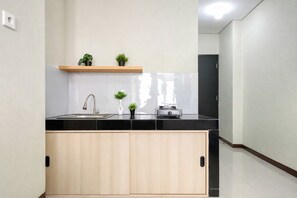 Cozinha com bancada preta, armários de madeira, pia de aço inoxidável, prateleira de madeira com plantas em vasos e eletrodoméstico preto.