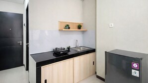 A modern kitchen with a black countertop, wooden cabinets, a built-in sink, and a small refrigerator. - Strategic And Neat Studio At Nifarro Park Apartment (Jakarta)