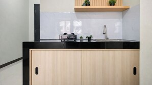 A modern kitchen with a black countertop, wooden cabinets, a built-in shelf with plants, and a stainless steel sink. - Strategic And Neat Studio At Nifarro Park Apartment (Jakarta)