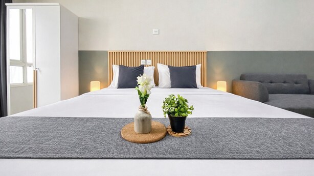 A hotel room with a bed, bedside lamps, a potted plant, and a window. - Strategic And Neat Studio At Nifarro Park Apartment (Jakarta)
