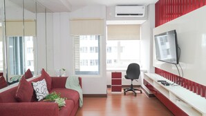 Um espaço de escritório moderno com um sofá vermelho, uma cadeira de escritório preta, uma TV na parede e um aparelho de ar condicionado.