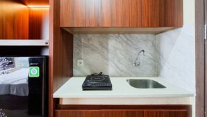 A compact kitchen with a marble backsplash, a built-in sink, and wooden cabinets. - Wooden Accents Studio For 2 Pax At Pacific Garden Campus Town Apartment (Tangerang)