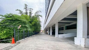 Un bâtiment doté d’un espace de stationnement couvert, d’un chemin en béton et de verdure sur le côté gauche.