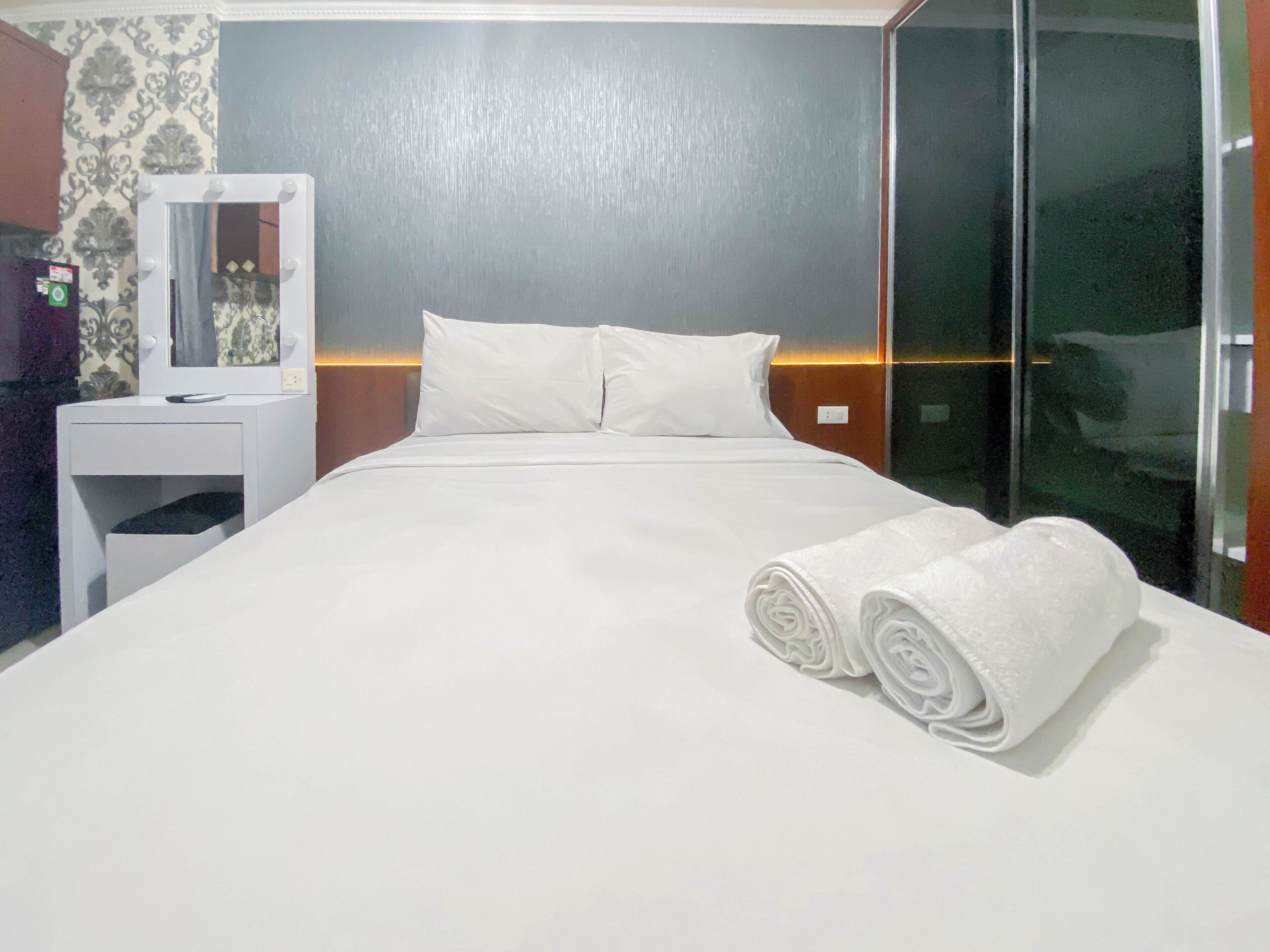 A hotel room with a neatly made bed, a bedside table with a mirror, and a wall with a patterned wallpaper.