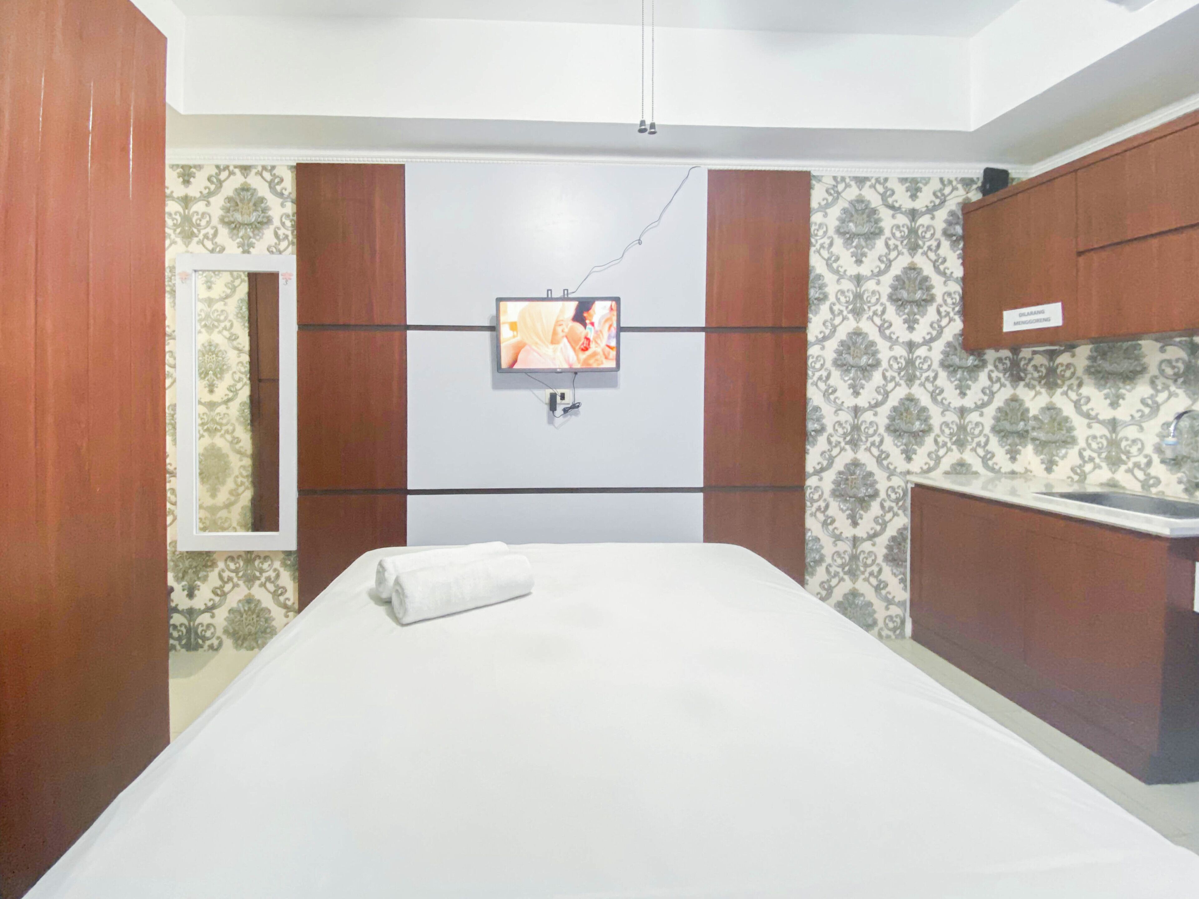 Quarto de hotel com cama, televisão presa na parede, banheiro com pia e papel de parede estampado.