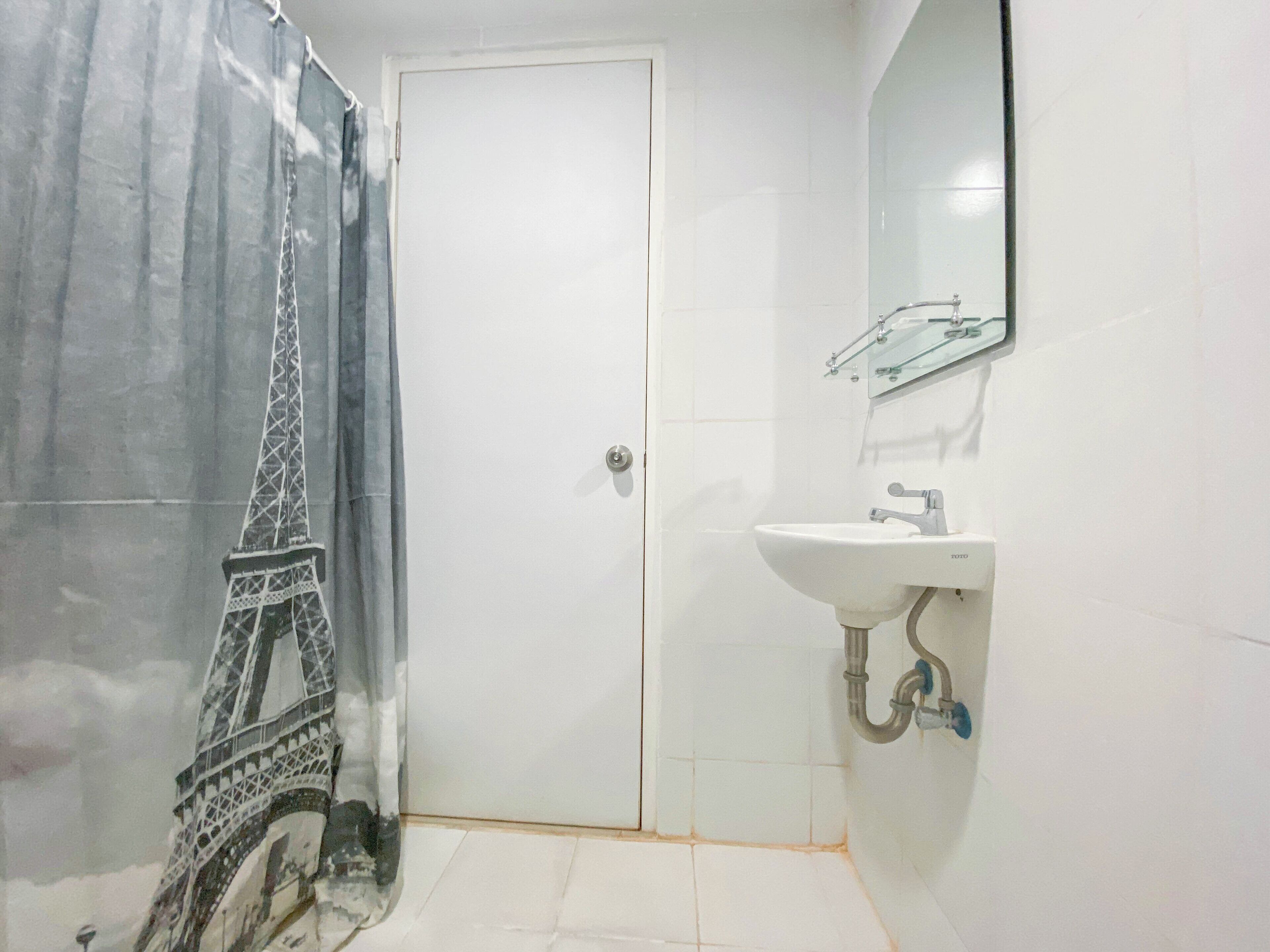 Ein Badezimmer mit weißer Tür, einer Duschvorhangs mit Eiffelturm-Motiv, einem Waschbecken mit Spiegel und gefliesten Wänden.