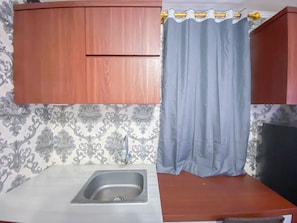 A compact kitchen with a single sink, wooden cabinets, and patterned wallpaper. - Simply And Homey Studio (No Kitchen) Room Apartment Paltrow City (Semarang)