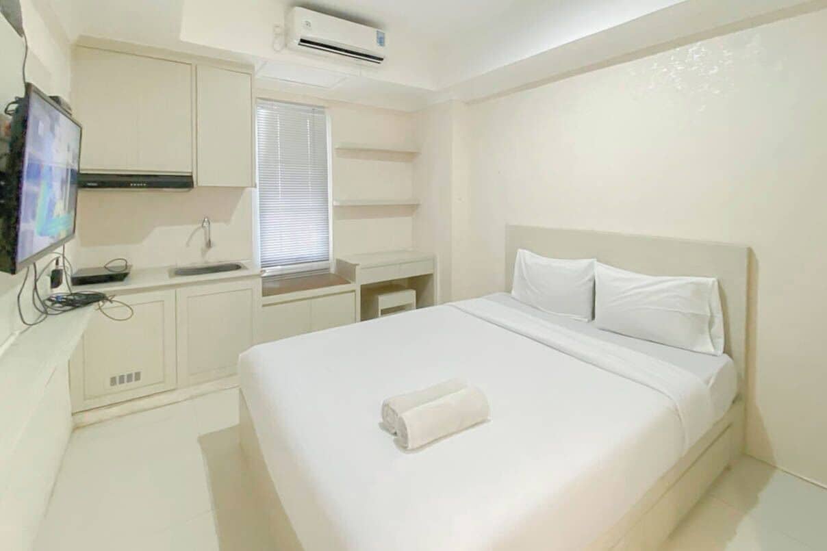A hotel room with a bed, a TV, a desk, and a window with blinds.