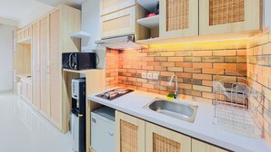 A compact kitchen with a brick backsplash, wooden cabinets, a built-in microwave, and a stainless steel sink. - Delightful Studio Space At Apartment Patraland Amarta (Ngaglik)