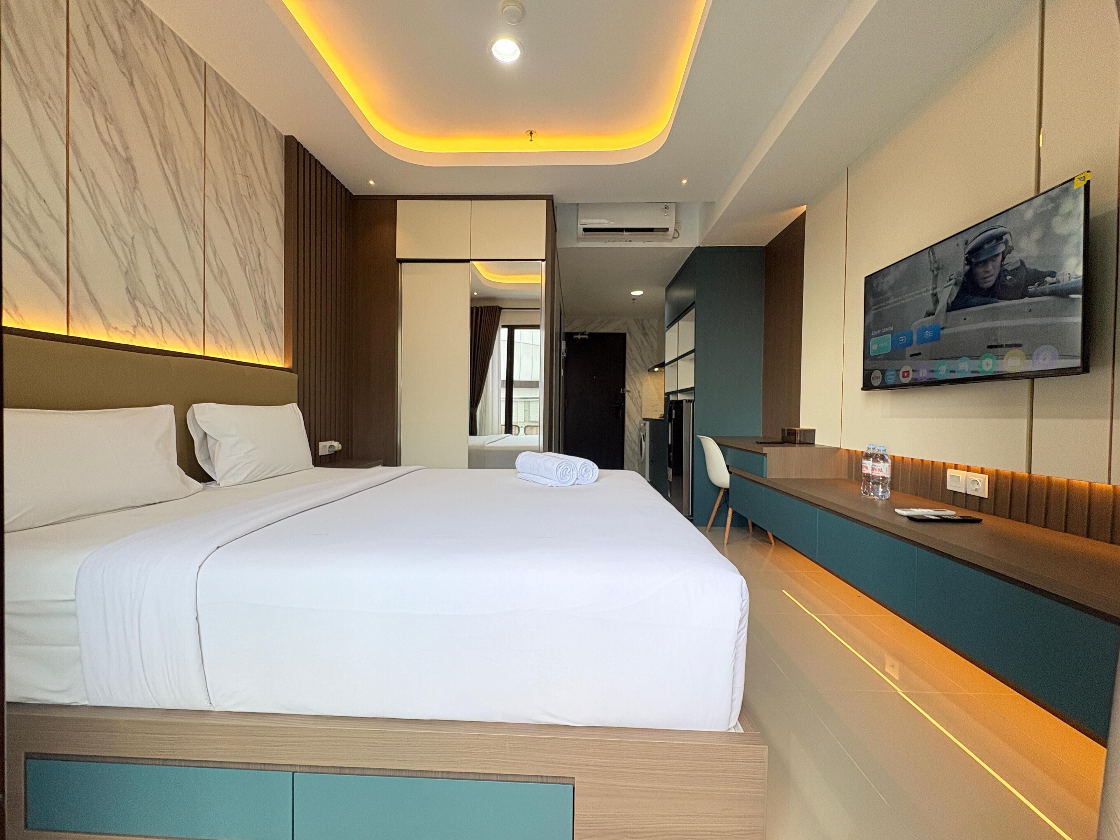 A modern hotel room with a large bed, a desk, a TV, and a bathroom visible through an open door.