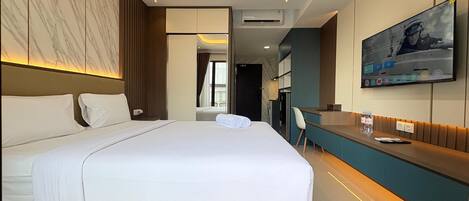 A modern hotel room with a large bed, a desk, a TV, and a bathroom visible through an open door.