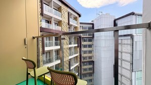 Un balcón con dos sillas y vistas a edificios cercanos, bajo un cielo despejado.