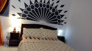Ein Schlafzimmer mit einem Bett, einer Wanddekoration, einem Nachttisch und einer Lampe.