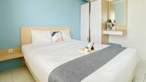 A neatly made bed with a grey throw, a bedside table with a vase, and a mirror above it. - Cozy With Blue Accent 2Br At Podomoro Golf View Apartment (Gunung Putri)