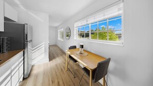 A modern kitchen with white cabinets, a wooden countertop, and a built-in refrigerator. There is a dining area with a wooden table and chairs, and a large window with a view of greenery. - Miami Retreat 1-BD - Parking and Gym (North Miami)
