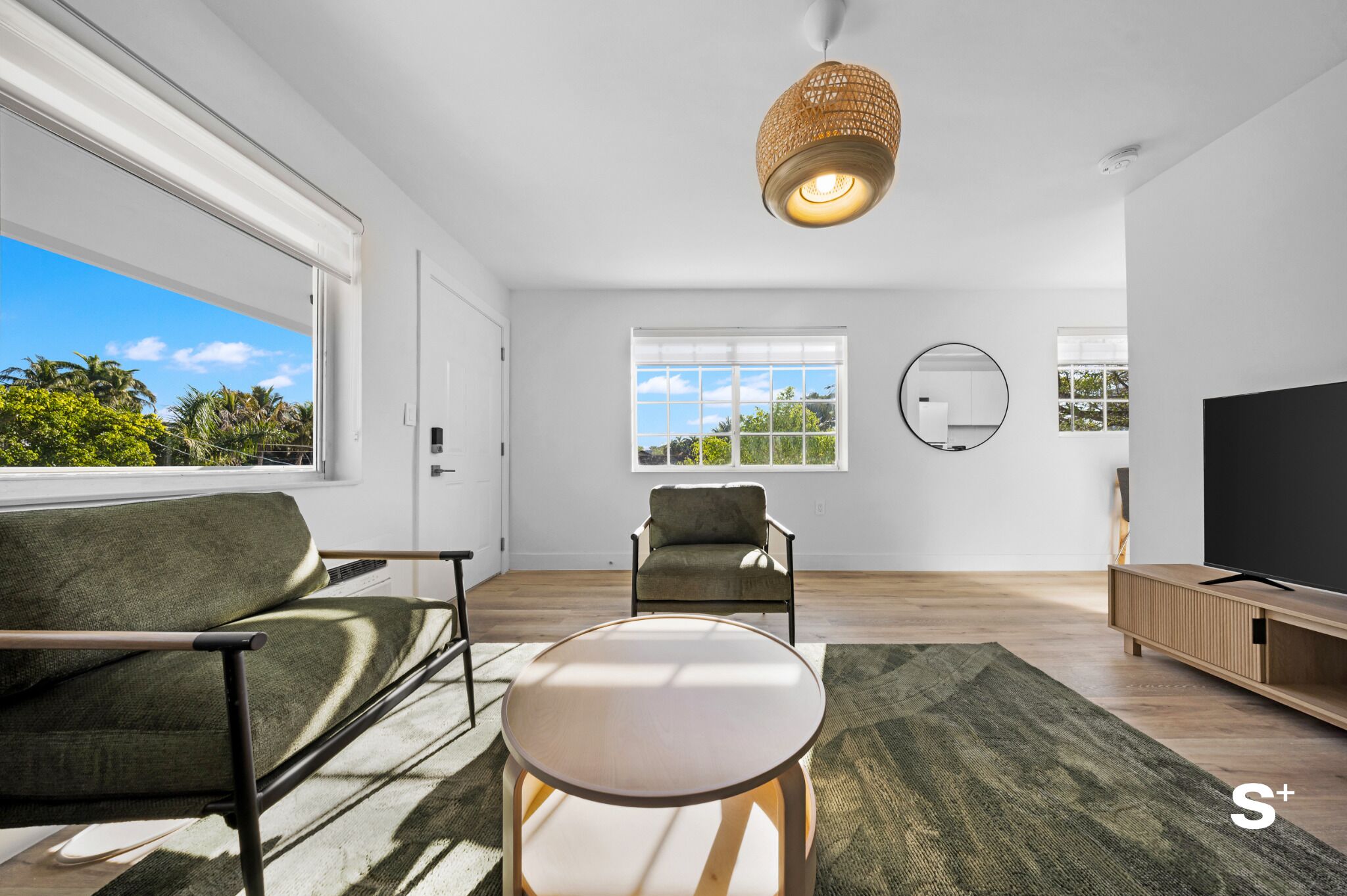 A modern living room with a sofa, armchair, round table, and a TV.