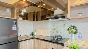 A modern kitchen with a refrigerator, stove, and wooden cabinets. - 2BR Corner with South and East View at Podomoro Golf View Apartment (Gunung Putri)