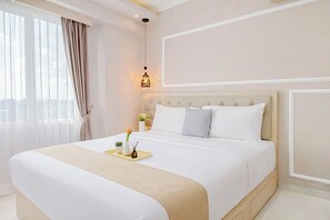 A hotel room with a large bed, a bedside table with a lamp, and a view through the window. - 2BR Corner with South and East View at Podomoro Golf View Apartment (Gunung Putri)