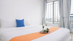 A hotel room with a bed, a window with curtains, and a view of buildings. - Simple Style Studio At Prima Orchard Apartment (Bekasi)