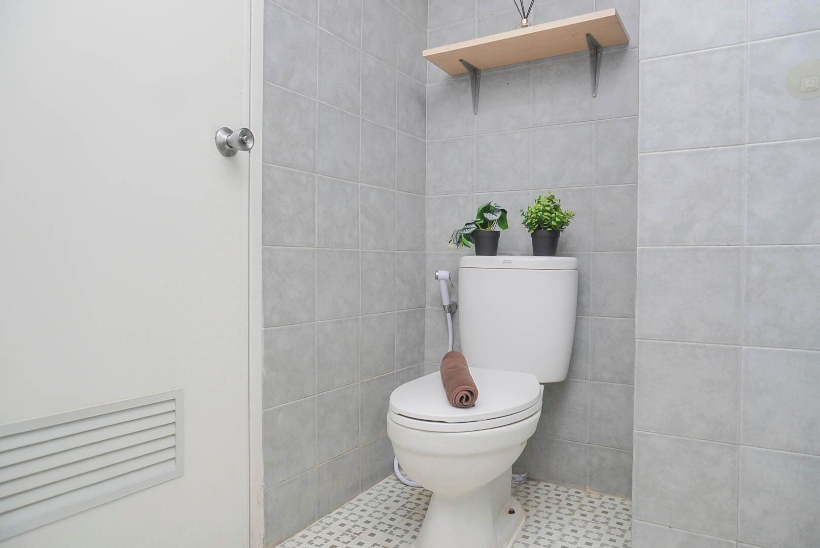 A bathroom with a toilet, a towel, and two potted plants on a shelf.