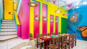 A brightly colored room with a staircase, a dining table with chairs, and a mural on the wall. - Maria Casa Malecon - Only Adults (Puerto Vallarta)